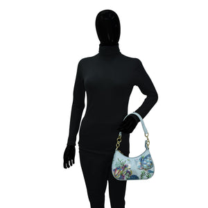 Mannequin wearing a black full-body suit and gloves, holding an Anuschka Small Convertible Hobo - 701 with a floral and butterfly design.