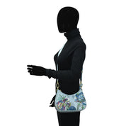 Mannequin with a black hoodie and gloves carrying an Anuschka Small Convertible Hobo - 701, isolated on a white background.