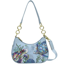 Load image into Gallery viewer, Light blue Anuschka Small Convertible Hobo - 701 with a colorful sea turtle and marine life design, featuring a gold chain strap and a white leather accent.
