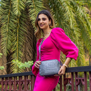 Woman in a pink dress posing with an Anuschka Twin Top Messenger - 704 featuring an adjustable strap outdoors.