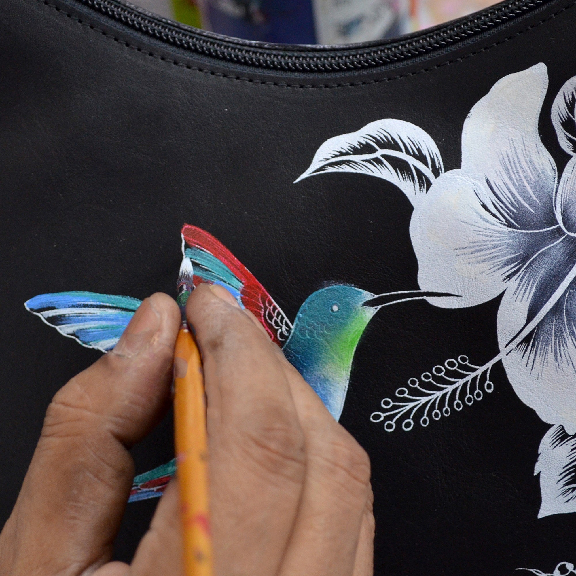 Hand painting a colorful hummingbird design on an Anuschka Flap Messenger Crossbody - 692.