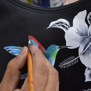 Hand painting a colorful hummingbird design on an Anuschka Flap Messenger Crossbody - 692.