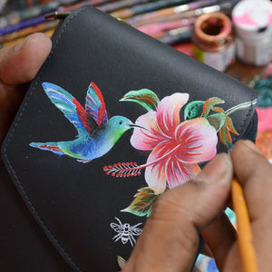 Hand painting a hummingbird and flowers on an Anuschka Crossbody Phone Case - 1173 with RFID protection.