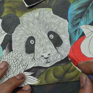 An artist's hands working on a detailed drawing of a panda for a wildlife organization using the Anuschka Everyday Shoulder Hobo - 670.