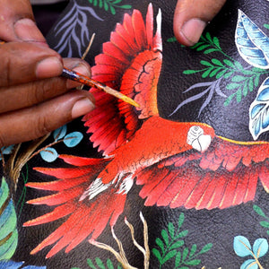 An artist's hand painting a detailed red bird on a dark, Anuschka Twin Top Messenger - 704, RFID protected surface.