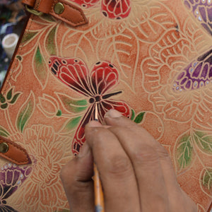 Hand painting a floral design on an Anuschka Accordion Flap Wallet - 1174 surface.