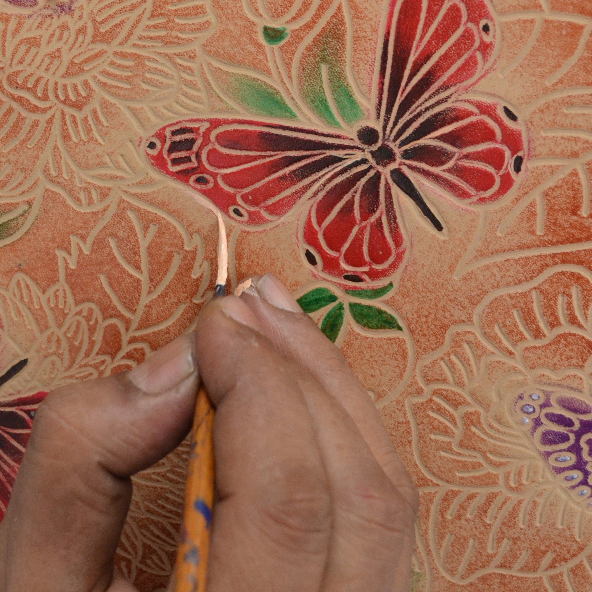 Artisan hand-carving a detailed pattern onto an Anuschka Classic Hobo With Studded Side Pockets - 433 genuine leather surface.